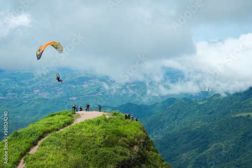 June 26 2020 : The tourist standing on the peak of hill watched flying paramotor Pilot flying from paramotor on over the sky at Pha Hua Sing Mountain, Phet Cha Boon province, Thailand.