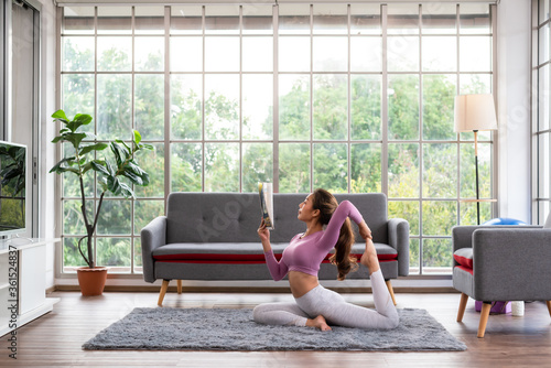 Young beautiful woman practicing yoga while reading magazine at home