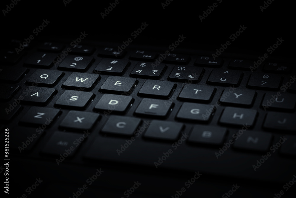 Closeup of black laptop QWERTY keyboard with light falling on keys.