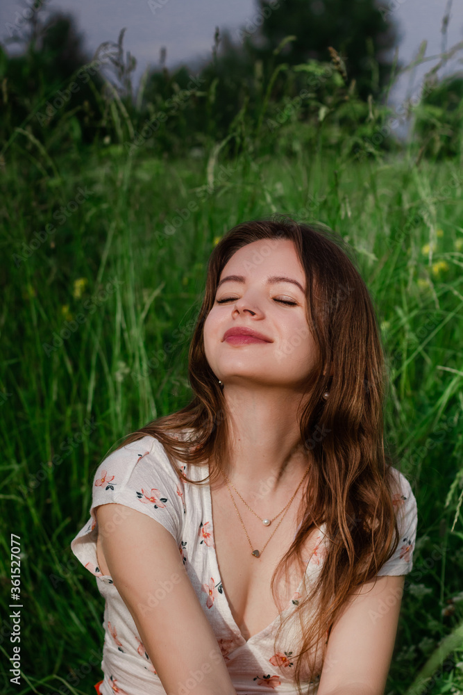 Soft focus close up of Young brunette girl in white top and sitting in green meadow field grass in countryside looking a side touching her hair and enjoy nature and rural life Solo out door activity Soft focus close up of Young brunette girl in white top and sitting in green meadow field grass in countryside looking a side touching her hair and enjoy nature and rural life Solo out door activity