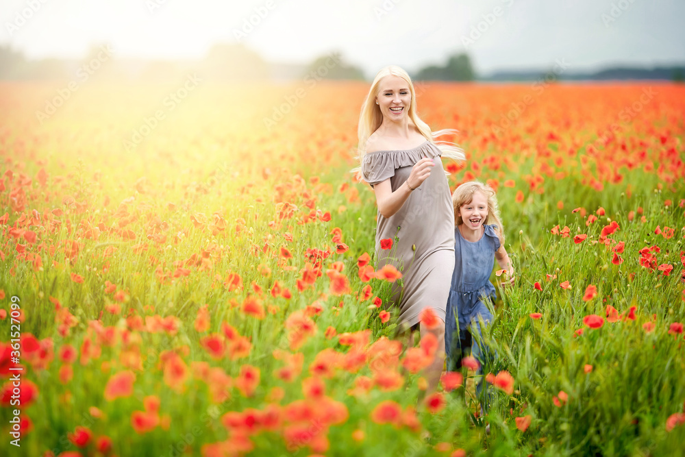 Happy family resting on a beautiful poppy field at sunset. Mom and daughter run around the meadow holding hands. family having fun. Happy family resting on a beautiful poppy field at sunset. Mom and daughter run around the meadow holding hands. family having fun.
