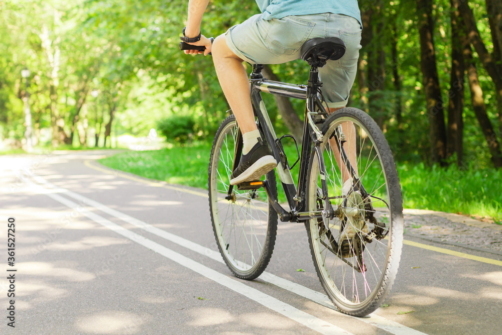 Obraz premium Man in blue t-shirt and blue jeans shorts cycling in the nature on bicycle on outdoor trail in park. Active summer solo outdoor activity. Concept of training, sport activity and health care.