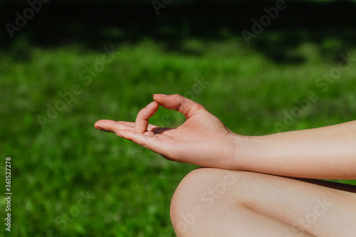Woman meditating and sitting in lotus pose on the green grass, holding her hand in om sign on her knee. Close up. Yoga practice. Solo outdoors activity. Yoga retreat. Healthy lifestyle. © P_Lila