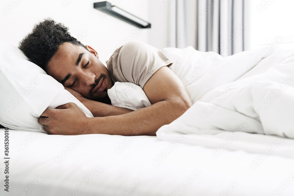 Photo of young african american man with mustache sleeping in white bed Photo of young african american man with mustache sleeping in white bed
