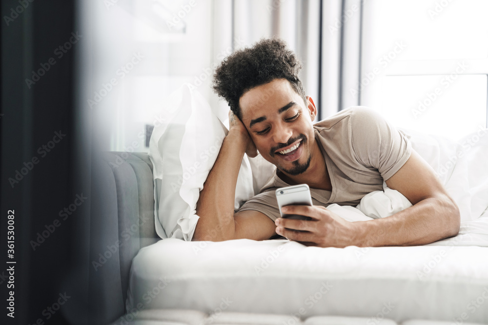 Photo of happy african american man using mobile phone and smiling