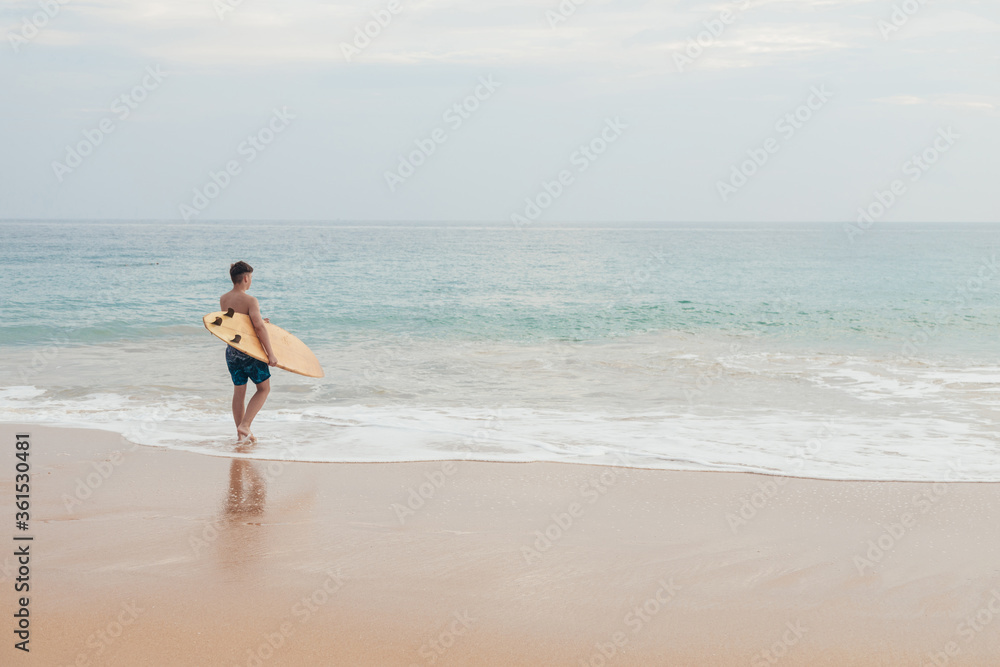 Handsome teenage boy with surfboard going into the ocean at sandy beach on surf line. Handsome teenage boy with surfboard going into the ocean at sandy beach on surf line.
