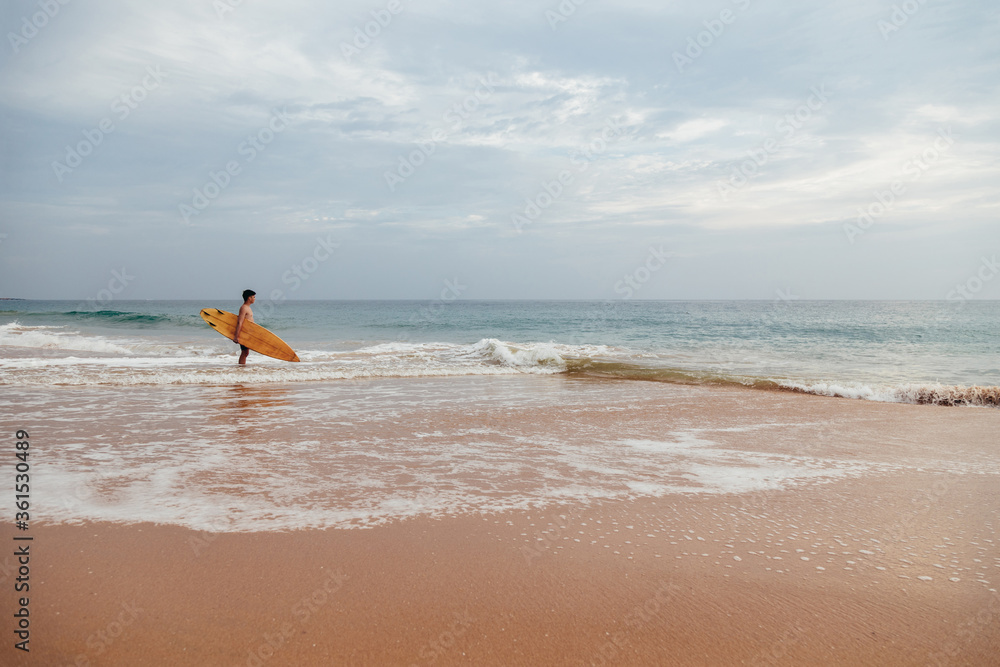 Handsome teenage boy with surfboard going into the ocean at sandy beach on foamy surf line. Handsome teenage boy with surfboard going into the ocean at sandy beach on foamy surf line.