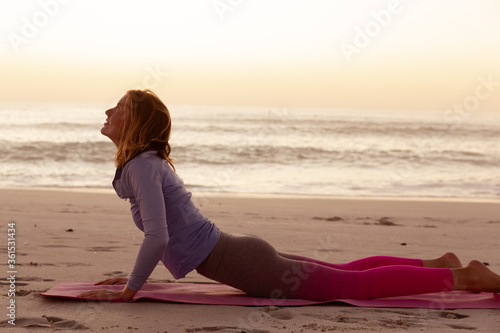 Woman performing yoga on the beach during sunset