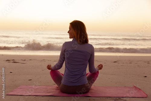 Rear view of woman performing yoga on the beach during sunset