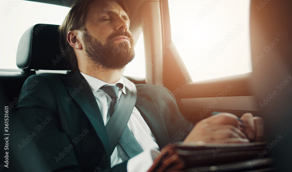 Bearded businessman with closed eyes and head leaned back sitting on backseat of car while traveling Bearded businessman with closed eyes and head leaned back sitting on backseat of car while traveling