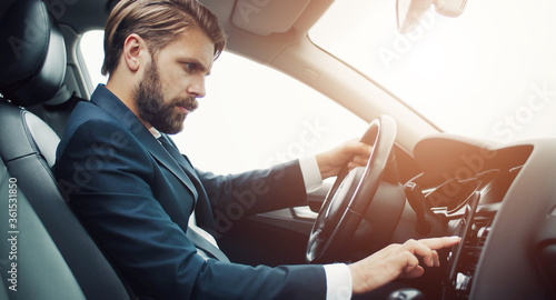 Side view of businessman setting up navigator or checking route on phone sitting in car behind wheel © MYDAYcontent