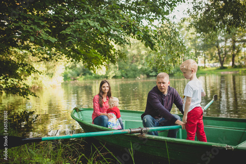 A family with a daughter and son swim in a park on a boat on the river. Dad helps, teaches his son to paddle. In the background mom with a small daughter. Family summer vacation concept, happy family.