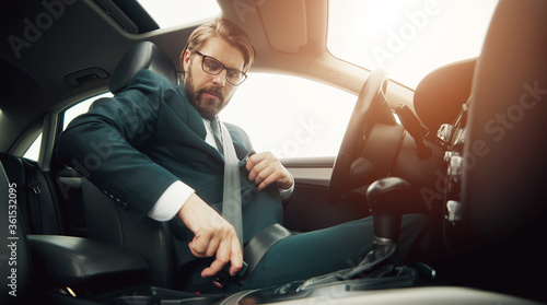Low angle of businessman sitting in car fastening seatbelt before driving caring about safety