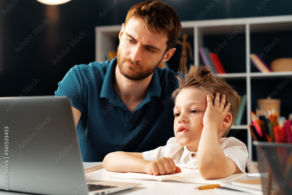 Young boy sitting with his father at the table and using laptop Young boy sitting with his father at the table and using laptop