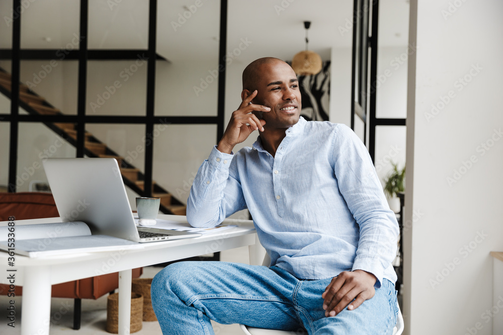 Fototapeta premium Photo of smiling man working with laptop while sitting at table