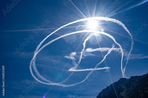 Fighter jet contrails chemtrails blue sky with sun in background  photo