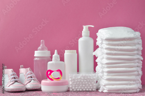Diapers and baby supplies on a pink background.