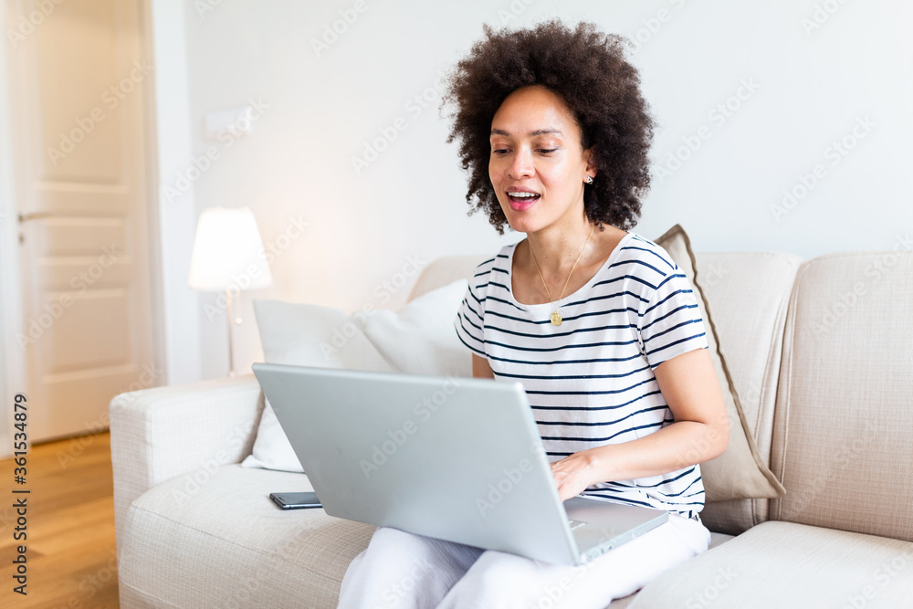 Young beautiful woman with curly hair working on laptop computer while sitting on the sofa at home, heck on oline shops for cyber monday sales. Technology woman concept alternative office freelance Young beautiful woman with curly hair working on laptop computer while sitting on the sofa at home, heck on oline shops for cyber monday sales. Technology woman concept alternative office freelance