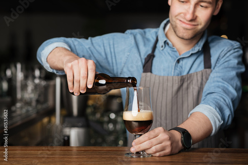 Repeat the order. Bartender in apron and denim shirt, pours dark beer in glass