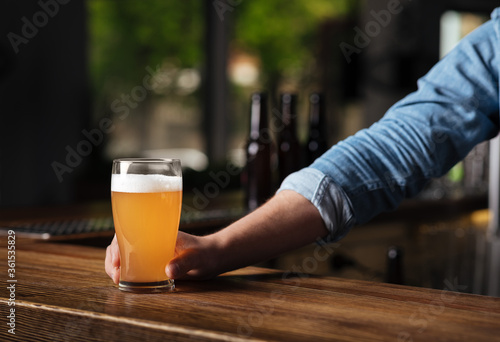 Oktoberfest in pub. Bartender hand holds lager beer in glass in interior of bar