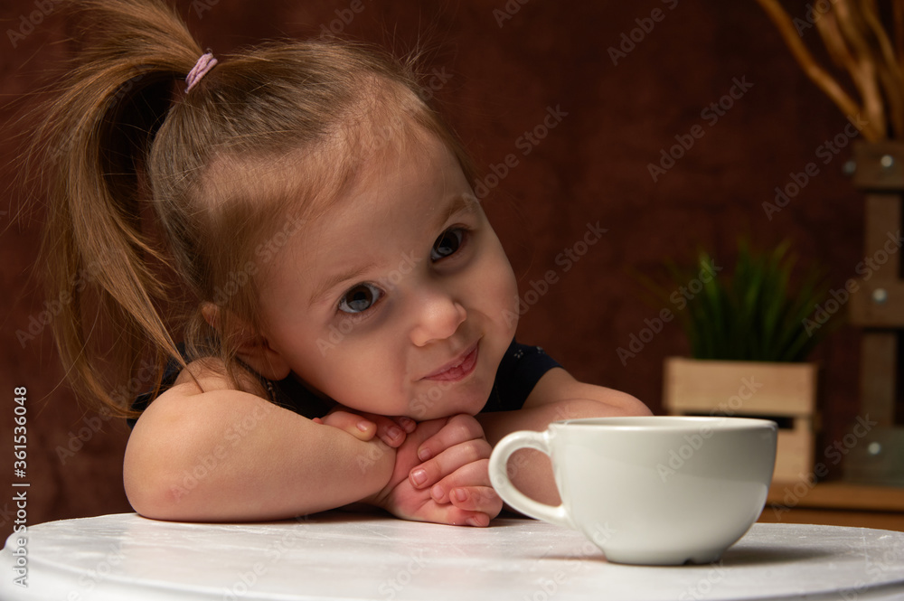 The little girl enthusiastically looks clasped hands on the table in anticipation of a miracle. The little girl enthusiastically looks clasped hands on the table in anticipation of a miracle.