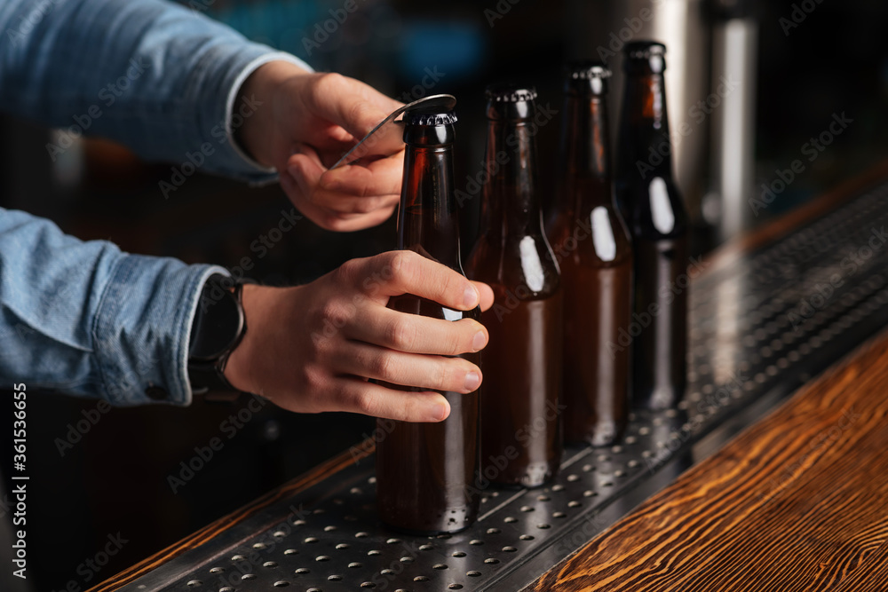 Bartender opens lot of glass bottles with lager on wooden bar counter