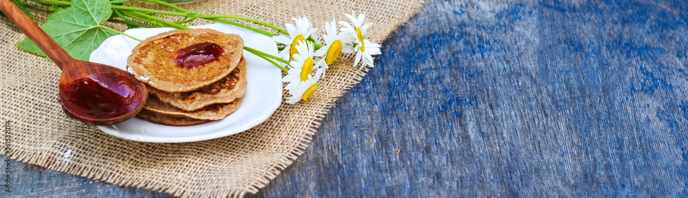 pancakes, tea with black currant on a green background. put jam on the pancakes. outdoors in a rustic style on a linen canvas fabric. next to daisies. long banner with copyspase pancakes, tea with black currant on a green background. put jam on the pancakes. outdoors in a rustic style on a linen canvas fabric. next to daisies. long banner with copyspase