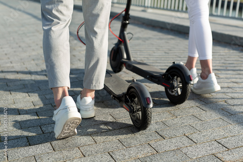 A couple of men and women are walking in the Park and pushing electric scooters © Artem Zakharov