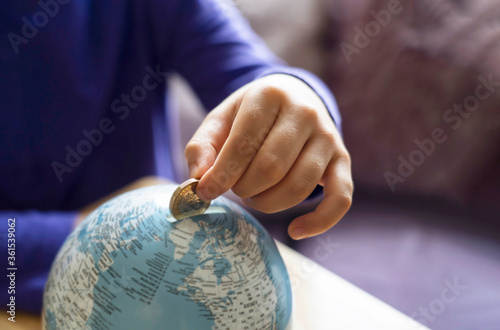 Kid hand putting one pound coin into piggy bank to donate money helping the earth, Hand holding money, Children learning to save money for sharing, studying, traveling or future with new normal life