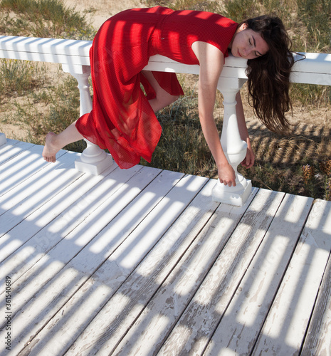 A young girl in a red dress is lying on the railing. Very tired. Funny pose of the model.