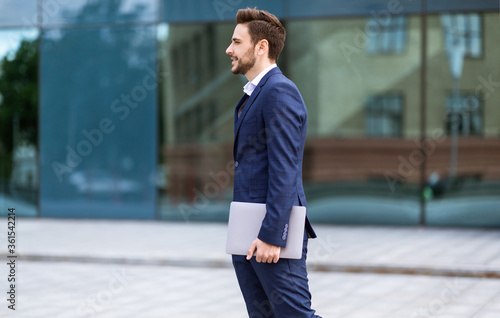 Successful trader in business suit holding tablet computer in central city area, side view