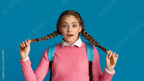 Cute teenager girl with backpack holding on pigtails