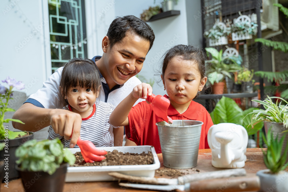 Asian father and two daughters are happy when using a shovel to grow potted plants to fill activities at home Asian father and two daughters are happy when using a shovel to grow potted plants to fill activities at home