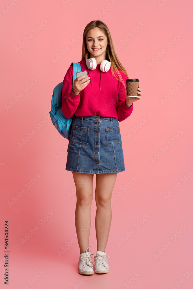 Modern teenage girl with cup of coffee, backpack and with headphones, checking for smartphone Modern teenage girl with cup of coffee, backpack and with headphones, checking for smartphone
