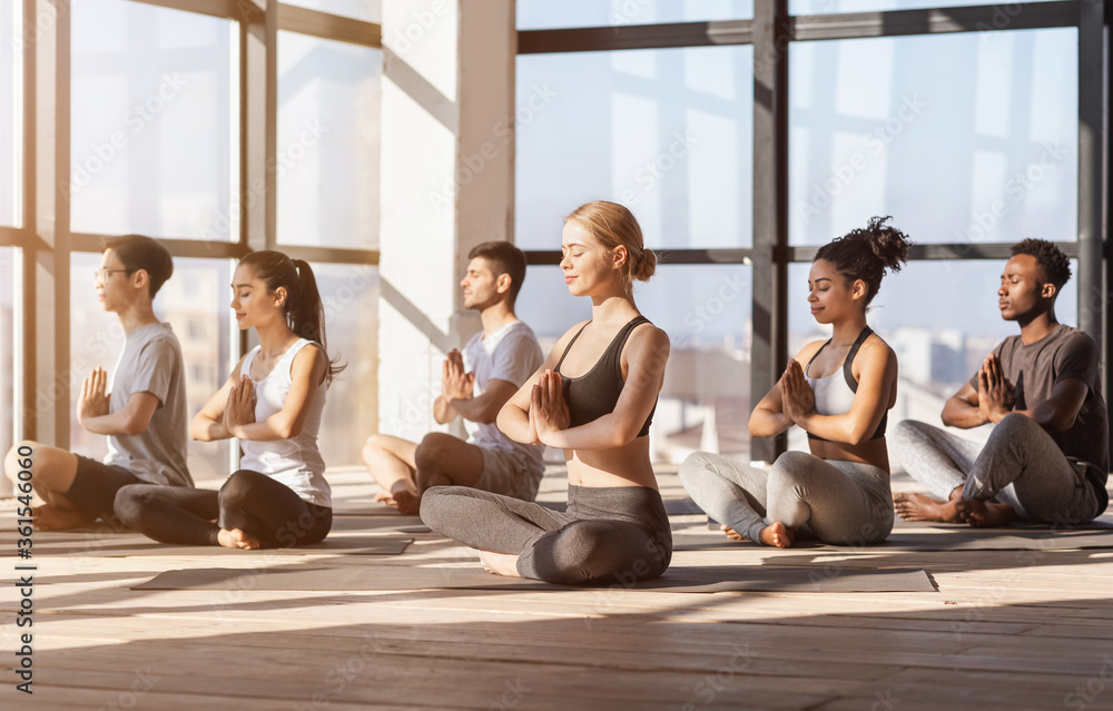 Fototapeta premium Meditation Session. Group Of Diverse Sporty People Practicing Yoga In Modern Gym