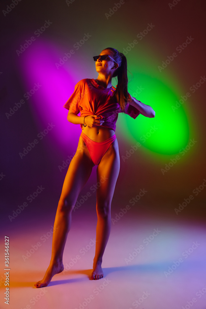 Fototapeta Seductive young girl' portrait isolated on bicolored neon studio background in neon. Fit sportive woman in bodysuit. Facial expression, summer, weekend, beauty, resort concept. Vacations.