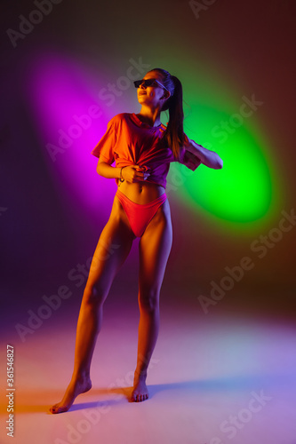 Seductive young girl' portrait isolated on bicolored neon studio background in neon. Fit sportive woman in bodysuit. Facial expression, summer, weekend, beauty, resort concept. Vacations. © master1305