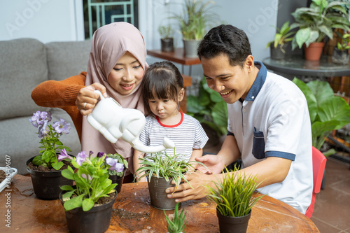 daughter sees her mother holding a watering can while watering plants and her father holding a potted plant on the terrace to take care of the plants