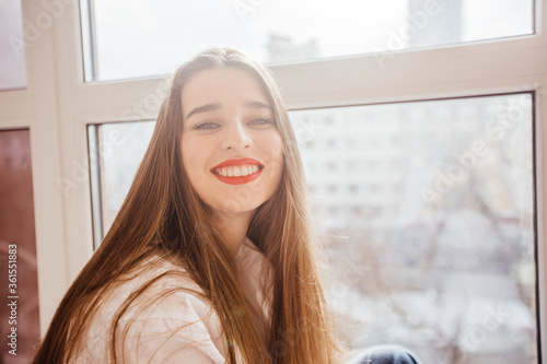 Free Download young beautiful girl sits at the window and smiles broadly - GFXLoad