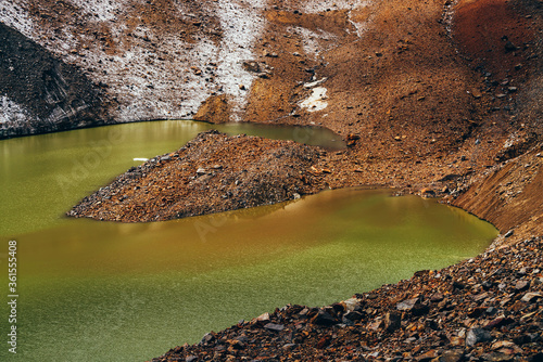 Stones on slope of glacier above mountain lake of acid green color. Beautiful emerald glacial lake and snowy slope of glacier with stones. Awesome alpine lake of unusual green tones. Amazing landscape