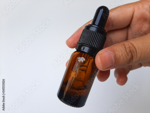 A hand holding a small glass pipette or dropper, that contain serum or skin care. Isolated in white background.