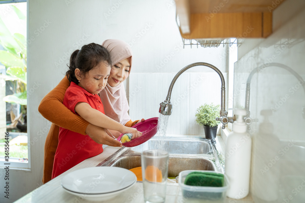 Helping hand. Cute little Girl Help Her muslim Mother In Washing Dishes At Family Kitchen Helping hand. Cute little Girl Help Her muslim Mother In Washing Dishes At Family Kitchen