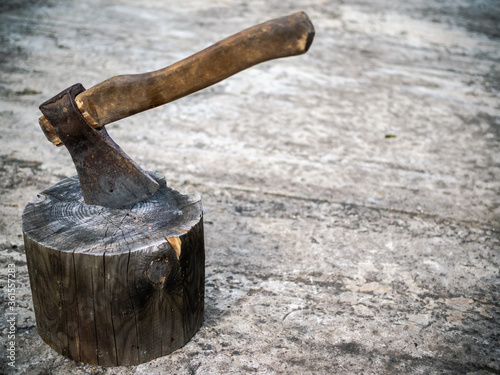 Vintage rusty сhopper in a block standing on a grey concrete floor left by lumberjack. Brutal image of an old iron axe with a wooden handle. 