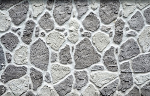 Exterior wall cladding made of irregular gray and white stones on concrete. Background and texture