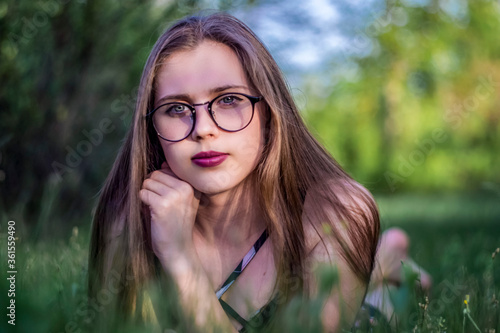 Portrait of a young girl with glasses in the green grass, bokeh effect.