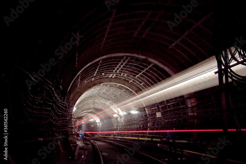 A passing train the lights of the metro tunnel.At the intersection of two metro lines.Goes into the tunnel.With red lines 