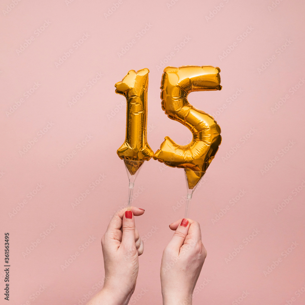 Obraz premium Female hand holding a number 15 birthday anniversary celebration gold balloon