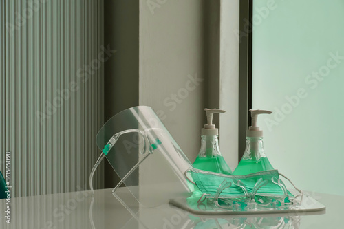 Transparent plastic faceshields, green sanitizers and green medical mask on white table in front of the glass door for wearing on face and rubbing hands, concept for anticoronavirus or covid-19. photo