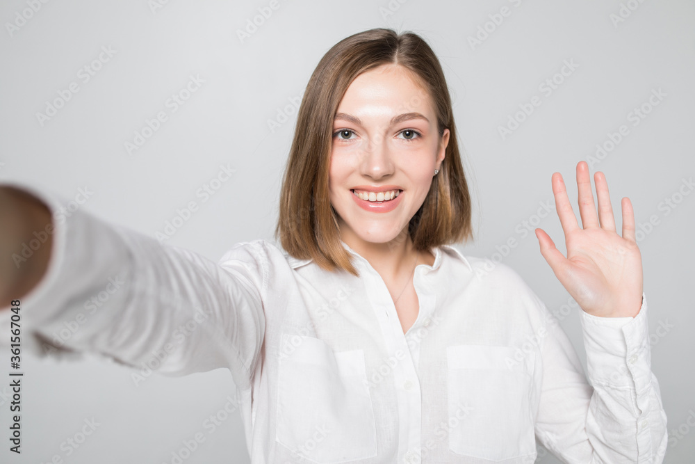 Portrait of smiling attractive woman taking a selfie while isolated over white background