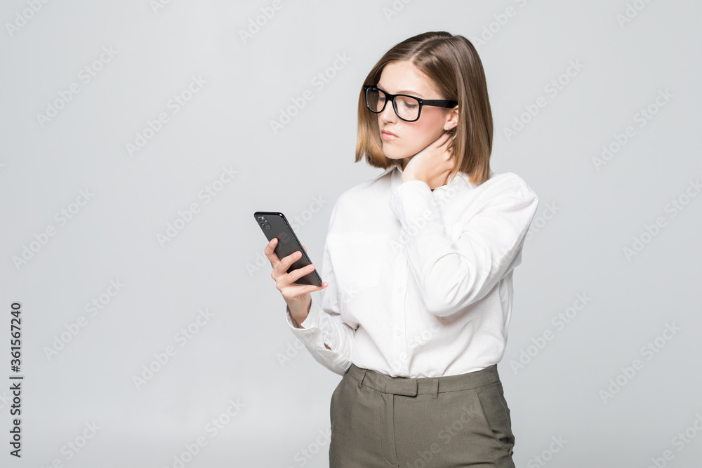 Young businesswoman looking in phone screen holding neck of pain isolated on white background